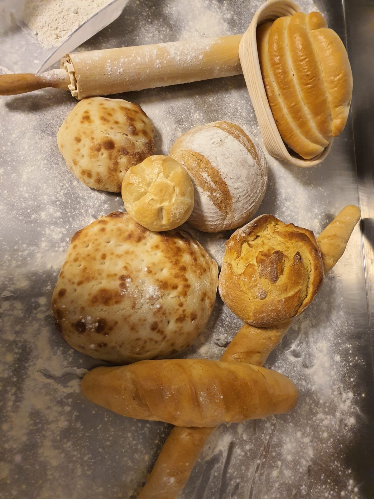 Verschiedene Brotlaibe und Gebäck auf einer bemehlten Arbeitsfläche mit Teigroller